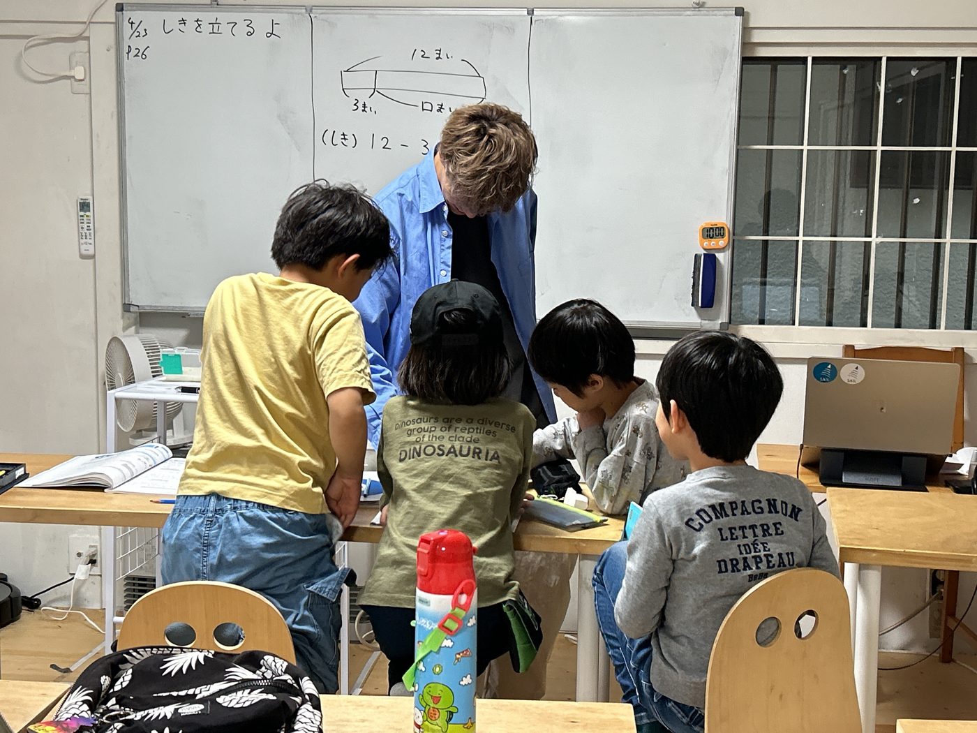 ホワイトボードの前の先生と、それを見る小学生たちの後ろ姿