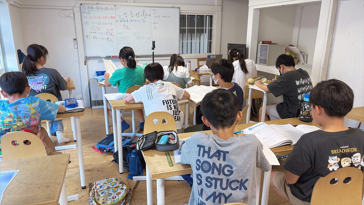 本店の教室。机に向かう子どもたちの後ろ姿と、板書の前に立つ先生
