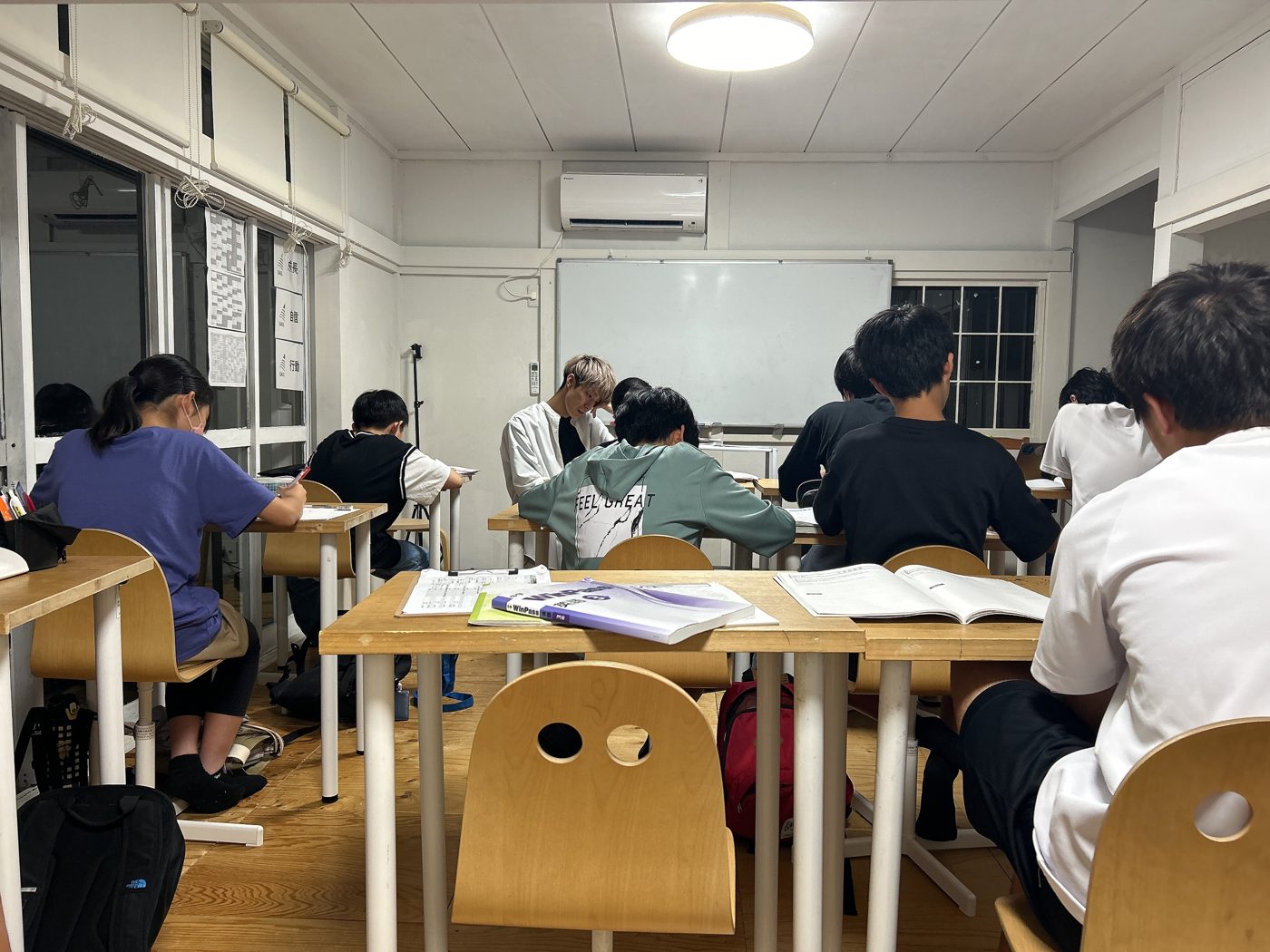 夜の教室で机に向かう中学生たちの後ろ姿と、ノートを見る先生