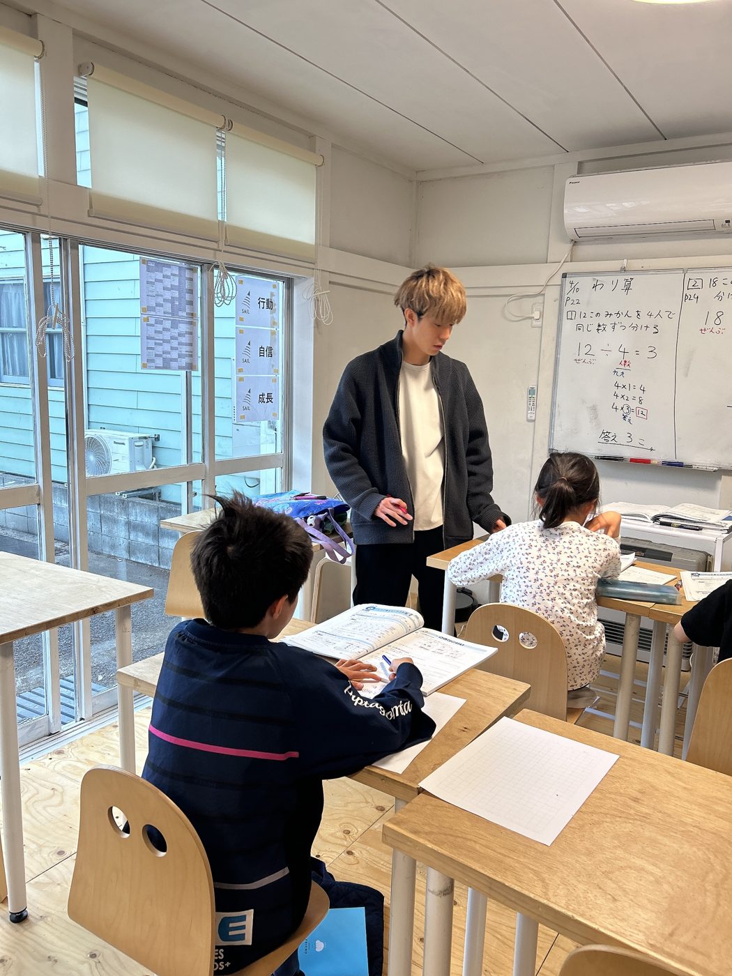 先生が机の横に立ち、子どもの手元を見ている